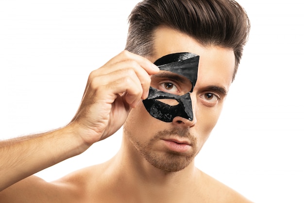 Young guy with a black charcoal mask on his face on white.