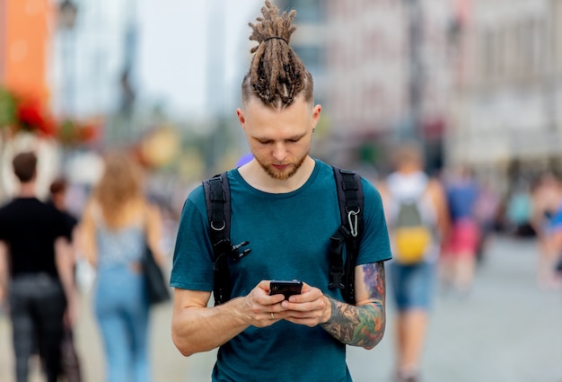 Young guy with dreadlocks is walking with a phone on the street