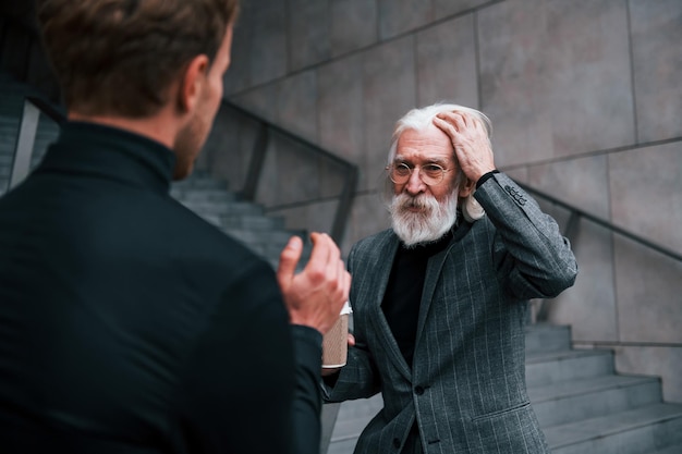 Young guy with senior man in elegant clothes is outdoors together Conception of business