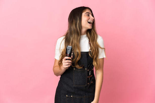 Young hairdresser woman isolated on pink wall laughing in lateral position