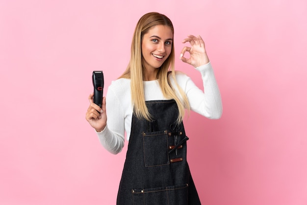 Young hairdresser woman isolated on pink wall showing ok sign with fingers