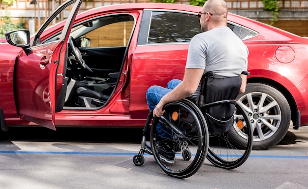 Young handicapped driver getting in red car fom wheelchair.