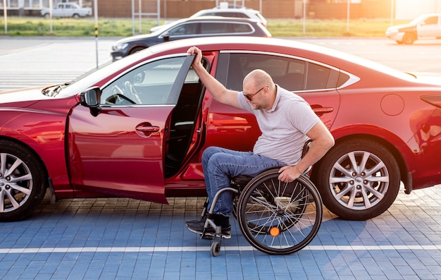 Young handicapped driver getting in red car fom wheelchair