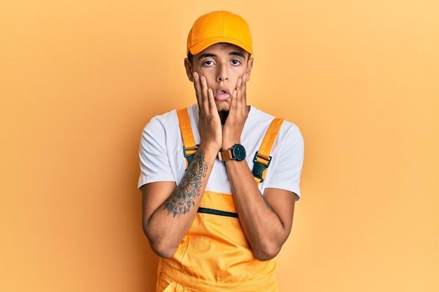 Young handsome african american man wearing handyman uniform over yellow background tired hands covering face depression and sadness upset and irritated for problem