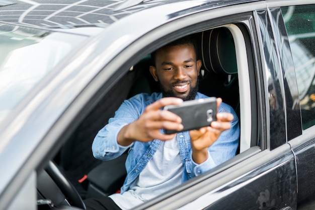 Young handsome african man take photo on the phone while drive his car