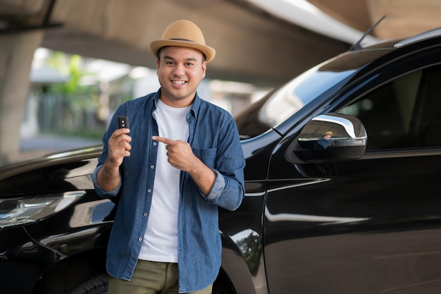 Young handsome asian man getting the new car.He showing car key and very happy. Buy or rent a car concept.