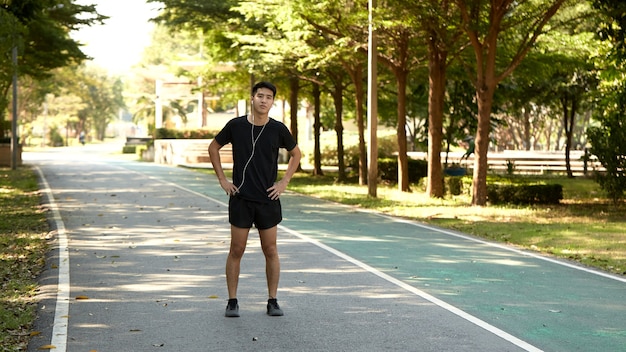 Young handsome Asian man jogging outdoors listening to music in the park