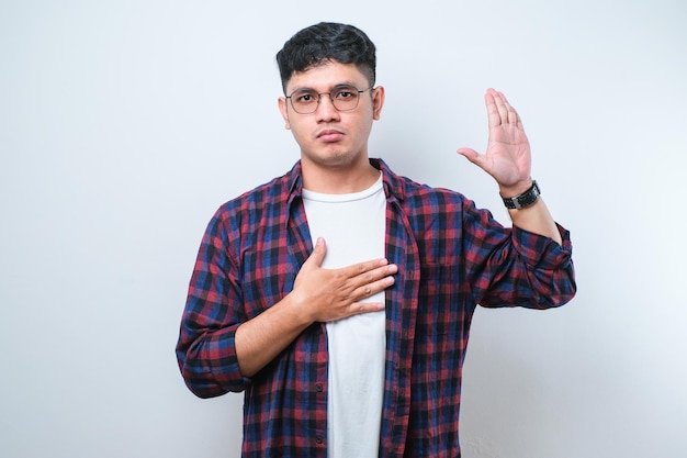 Young handsome asian man smiling swearing with hand on chest and fingers up making a loyalty promise oath