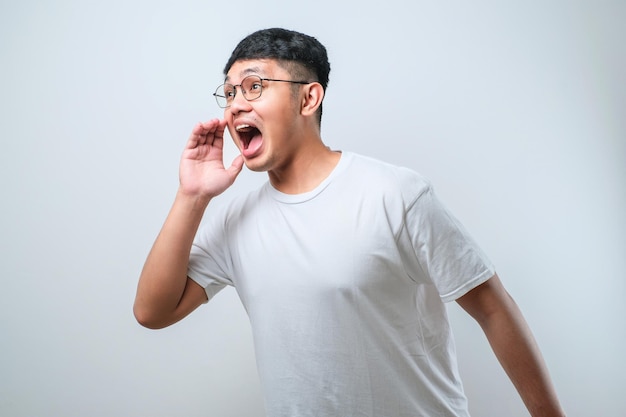 Young handsome asian man wearing casual shirt and glasses style shouting and screaming loud to side with hand on mouth