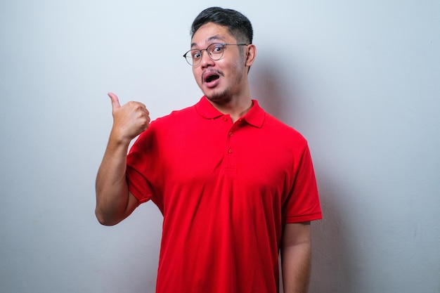 Young handsome asian man wearing casual shirt pointing something on his side with his hand