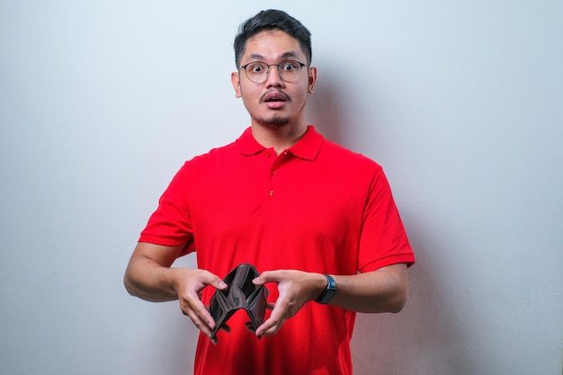 Young handsome Asian man wearing casual shirt showing empty wallet with shocked face expression surprised and speechless