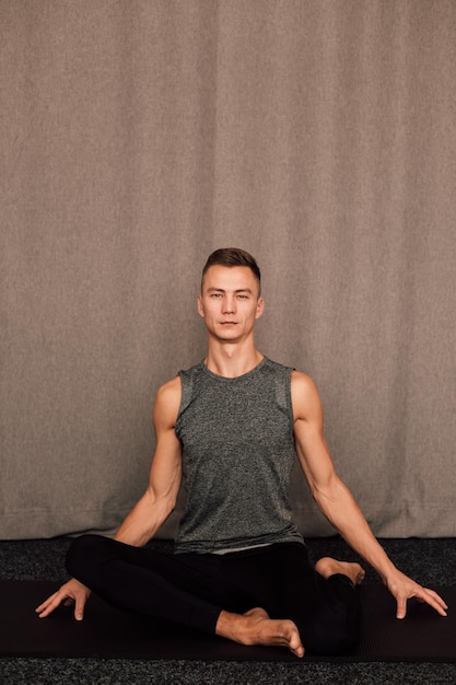 Young handsome athlete sits in the lotus position indoors