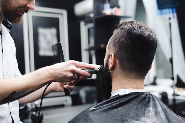 Young handsome barber making haircut of attractive man in barbershop.