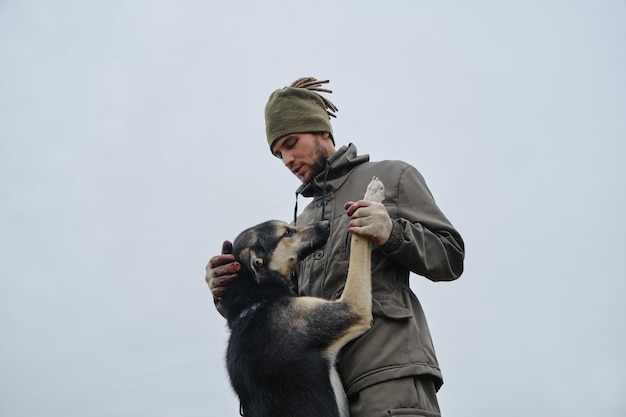 Young handsome bearded Caucasian man chooses mongrel dog in animal shelter