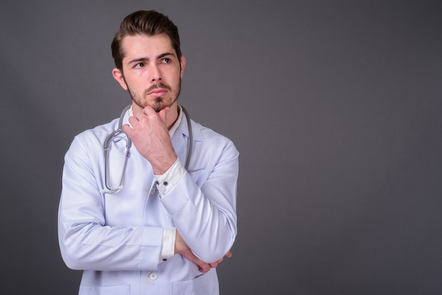 Young handsome bearded doctor against gray wall