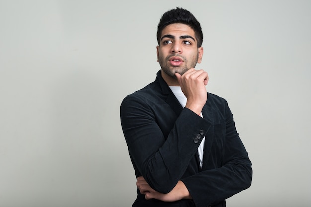 young handsome bearded Indian businessman against white wall