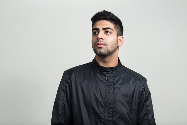 young handsome bearded Indian man with leather jacket as rock concept against white wall