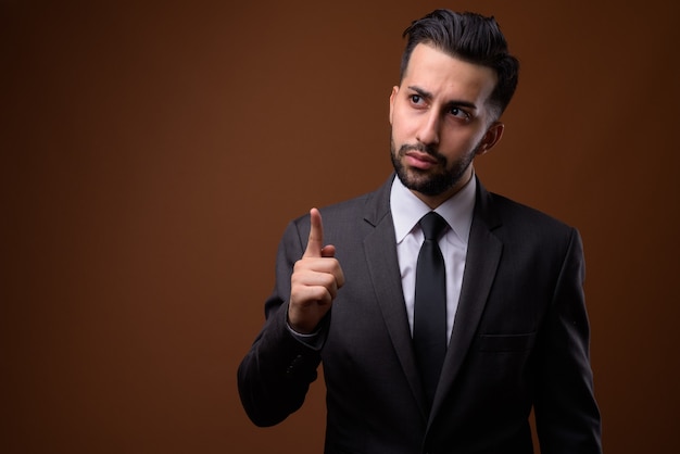 Young handsome bearded Iranian businessman against brown wall