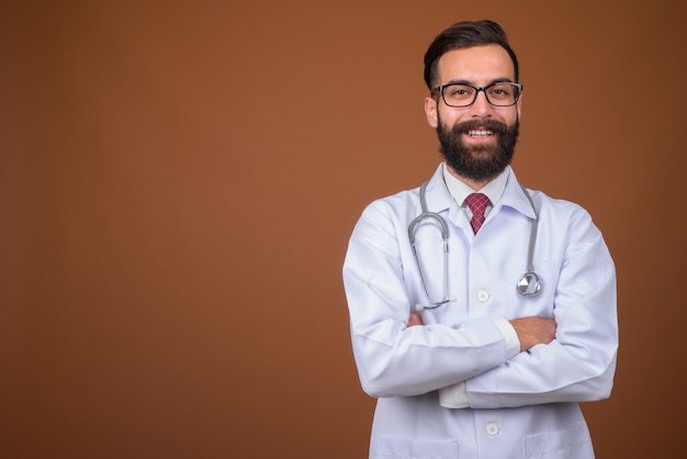 Photo young handsome bearded persian man doctor on brown wall