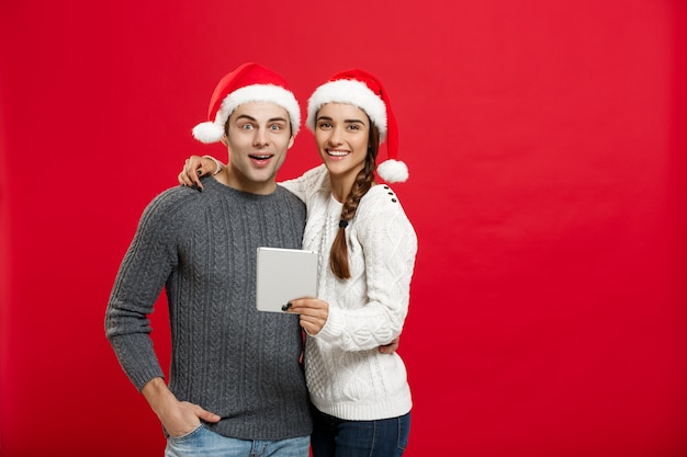 Young handsome and beautiful couple enjoy playing on tablet in christmas day.