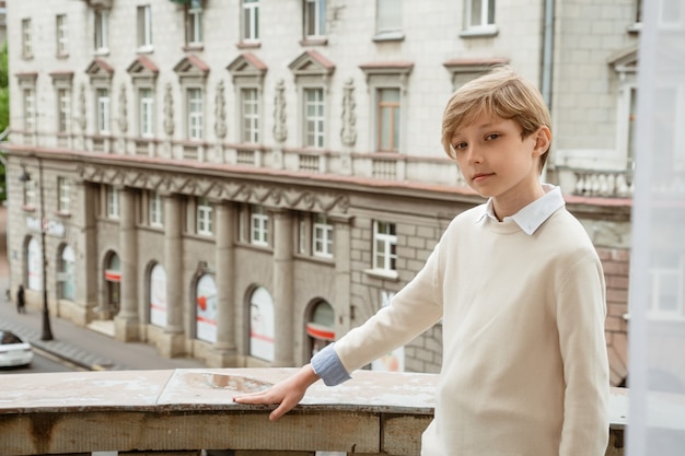 Young handsome blond guy in beige sweater posing on the balcony