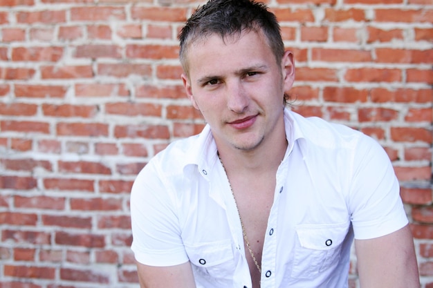 Young handsome blond guy in a white shirt stands near an old brick wall