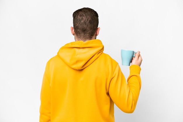 Young handsome blonde man holding cup of coffee over isolated background in back position