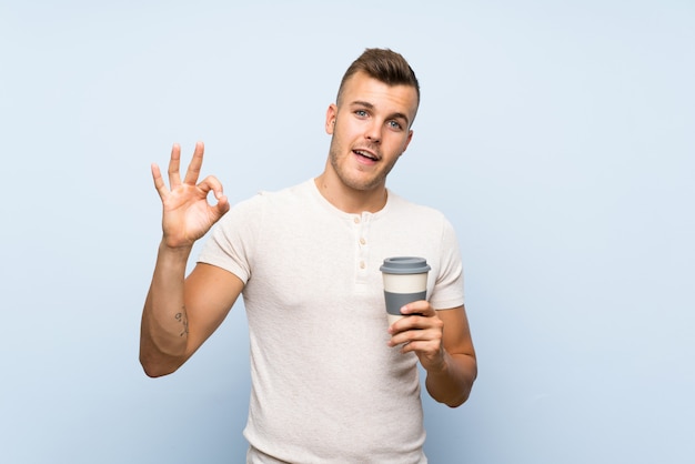 Young handsome blonde man holding hot cup of coffee