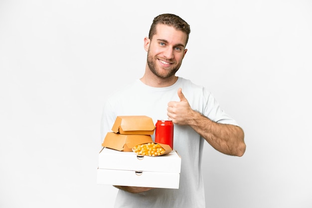 Young handsome blonde man holding pizzas and burgers over isolated background giving a thumbs up gesture