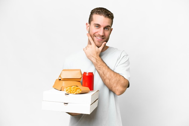 Young handsome blonde man holding pizzas and burgers over isolated background happy and smiling