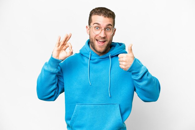 Young handsome blonde man over isolated white background showing ok sign and thumb up gesture