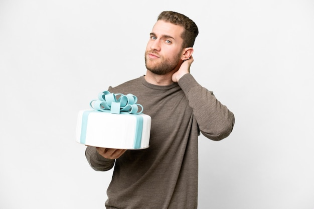 Young handsome blonde man with a big cake over isolated white background having doubts