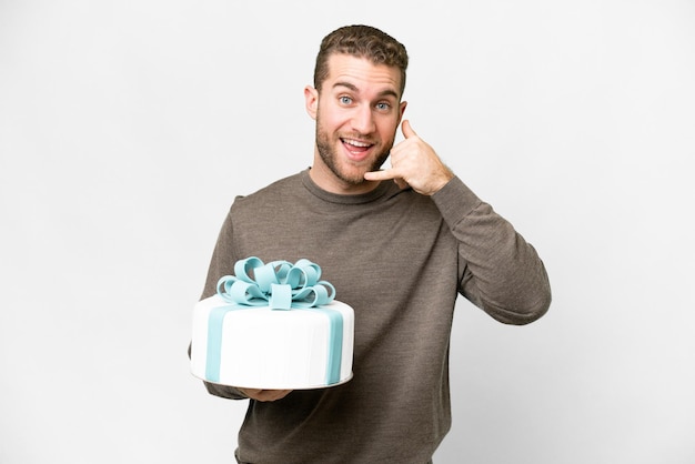 Young handsome blonde man with a big cake over isolated white background making phone gesture Call me back sign