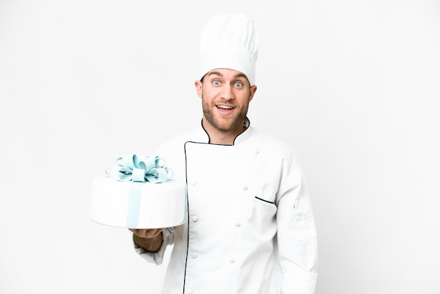 Young handsome blonde man with a big cake over isolated white background with surprise and shocked facial expression