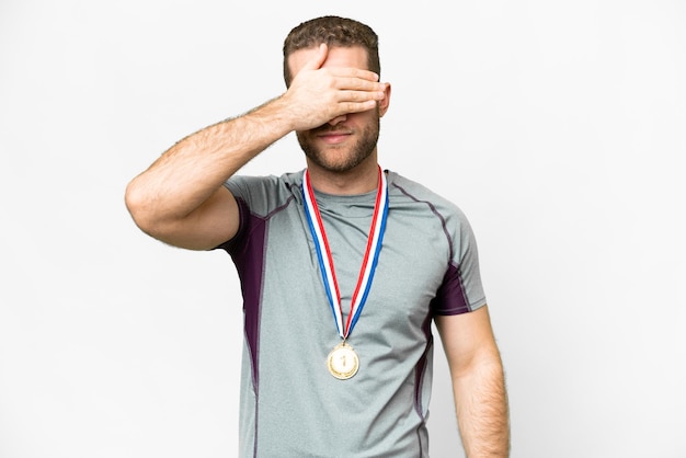 Young handsome blonde man with medals over isolated white background covering eyes by hands Do not want to see something