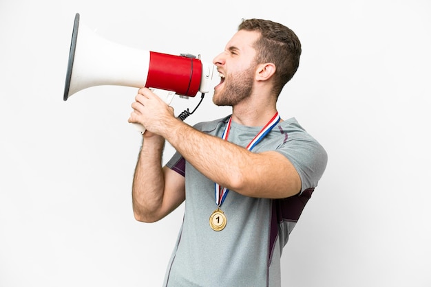 Young handsome blonde man with medals over isolated white background shouting through a megaphone