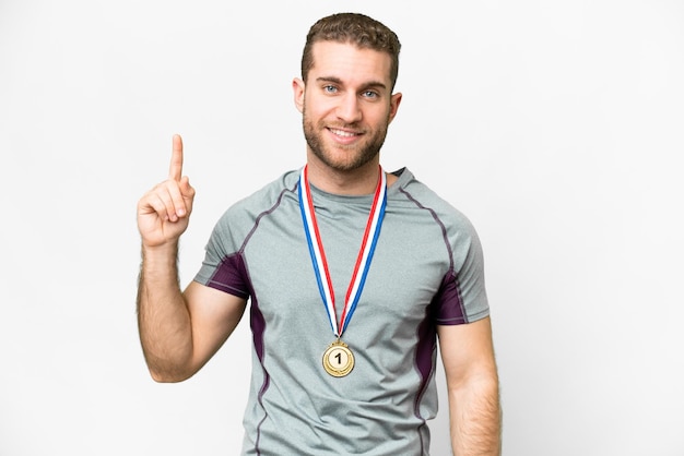 Young handsome blonde man with medals over isolated white background showing and lifting a finger in sign of the best