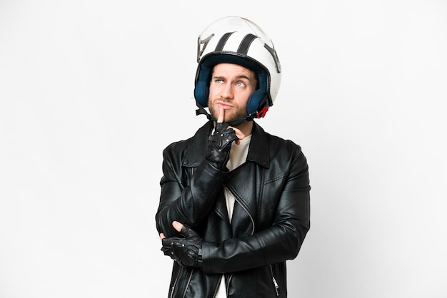 Young handsome blonde man with a motorcycle helmet over isolated white background having doubts while looking up