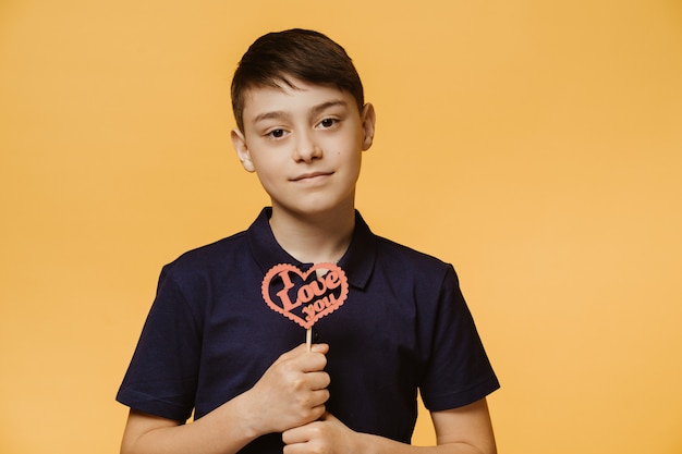 Young handsome boy dressed in a dark blue t-shirt, holds hand crafted heart with i love you inscription on it. Happy valentine . People sincere emotions.