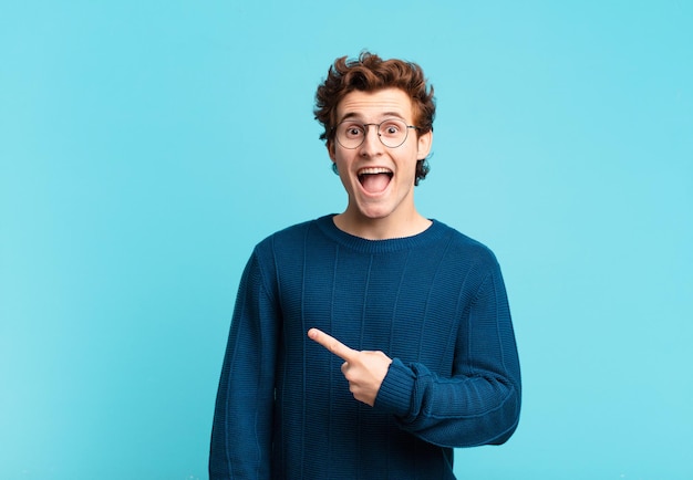 Young handsome boy looking excited and surprised pointing to the side and upwards to copy space