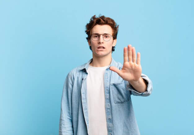 Young handsome boy looking serious, stern, displeased and angry showing open palm making stop gesture