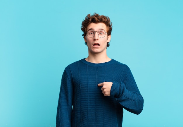 Young handsome boy looking shocked and surprised with mouth wide open, pointing to self