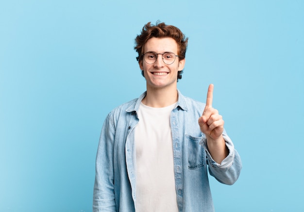 Young handsome boy smiling and looking friendly, showing number one or first with hand forward, counting down