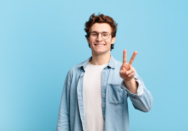 Young handsome boy smiling and looking happy, carefree and positive, gesturing victory or peace with one hand