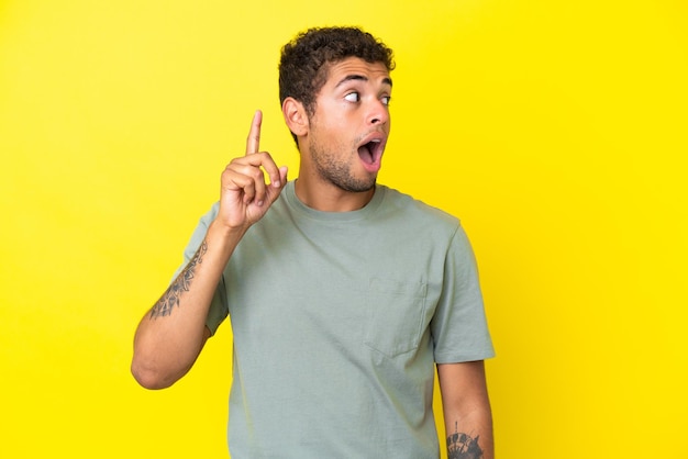 Young handsome Brazilian man isolated on yellow background intending to realizes the solution while lifting a finger up