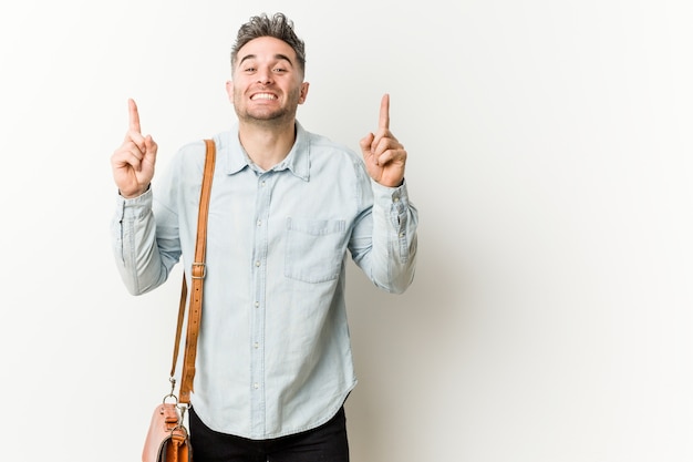 Young handsome business man indicates with both fore fingers up showing a blank space.