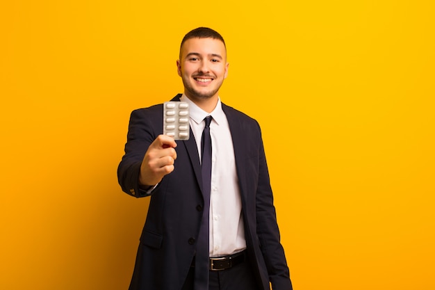 Young handsome businessman  against flat wall with pills capsules