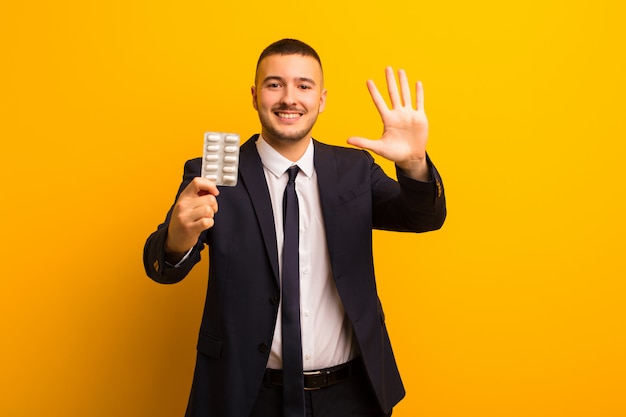 Young handsome businessman  against flat wall with pills capsules