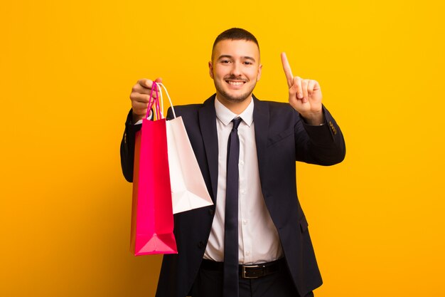 Young handsome businessman  against flat wall with shopping bags