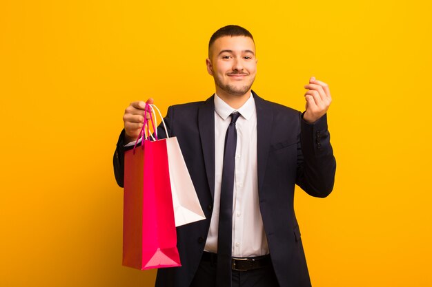 Young handsome businessman  against flat wall with shopping bags